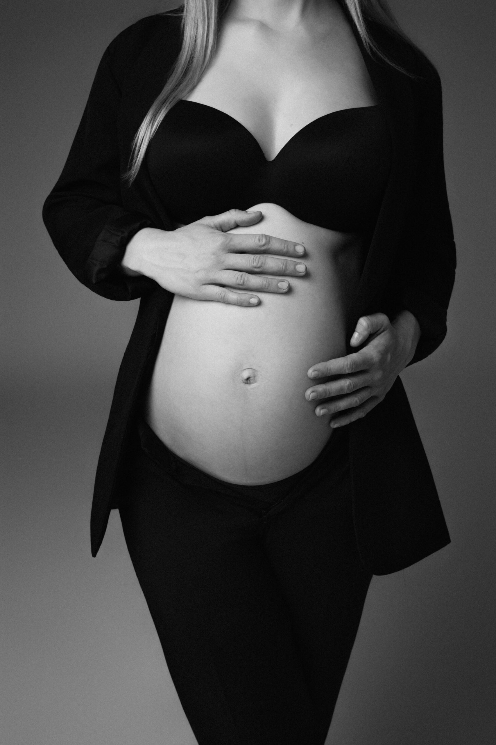 Schwarzweiß-Detailaufnahme eines Babybauchs mit liebevoll aufgelegten Händen bei einem Schwangerschaftsshooting in Ulm.