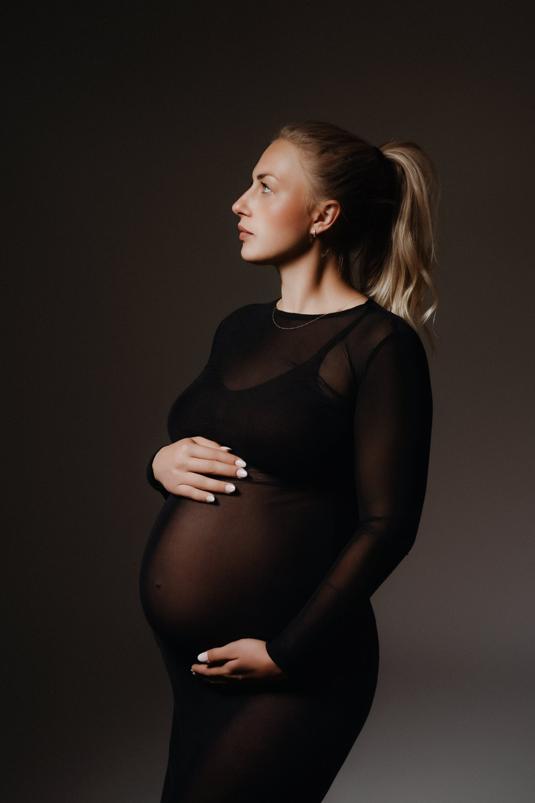 Werdende Mutter bei einem professionellen Schwangerschaftsshooting in Ulm mit schwarzem Kleid und Babybauch im Profil.