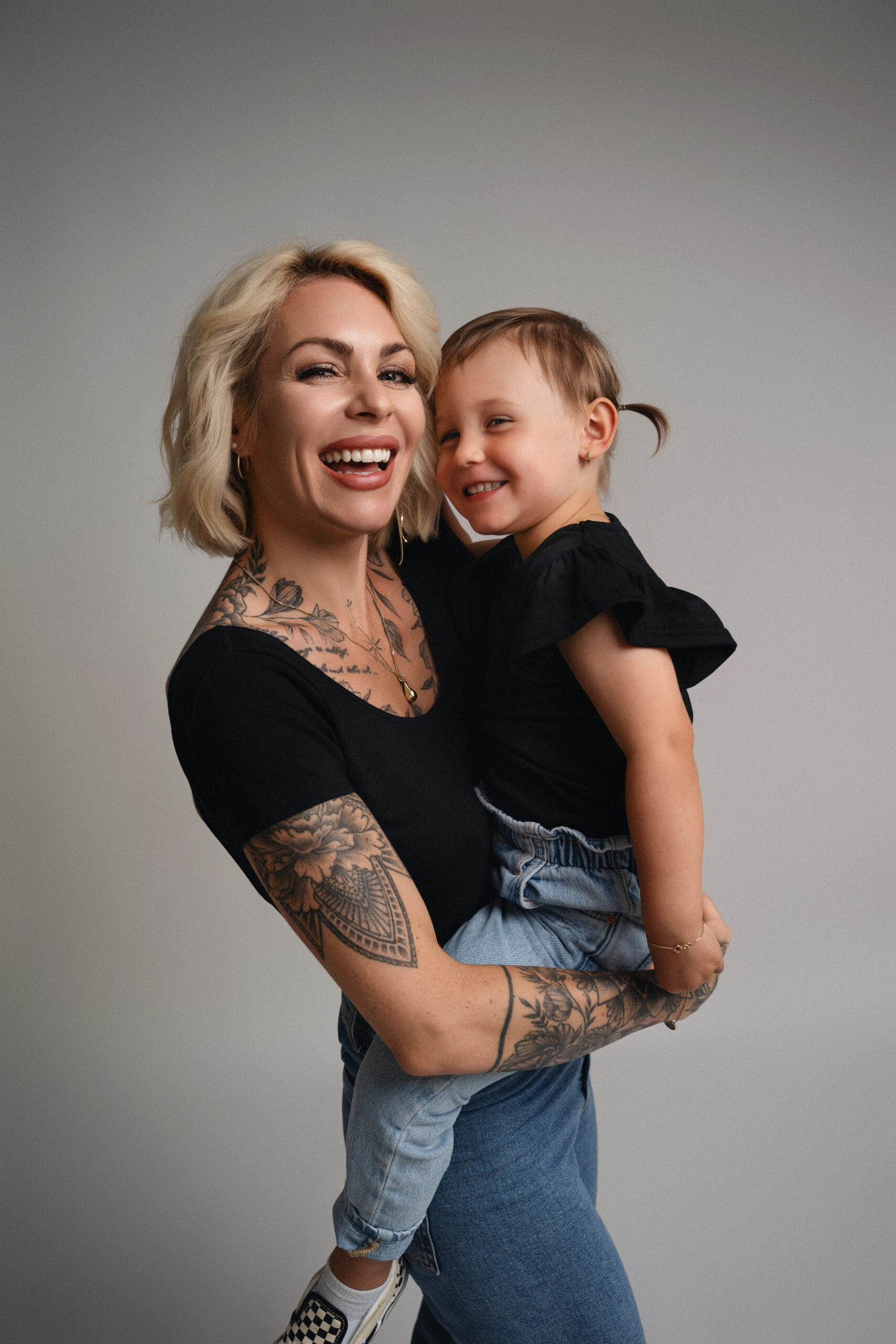 Glückliche Mutter mit ihrer Tochter beim emotionalen Mama-Tochter-Fotoshooting im Fotostudio, beide lachen in die Kamera.