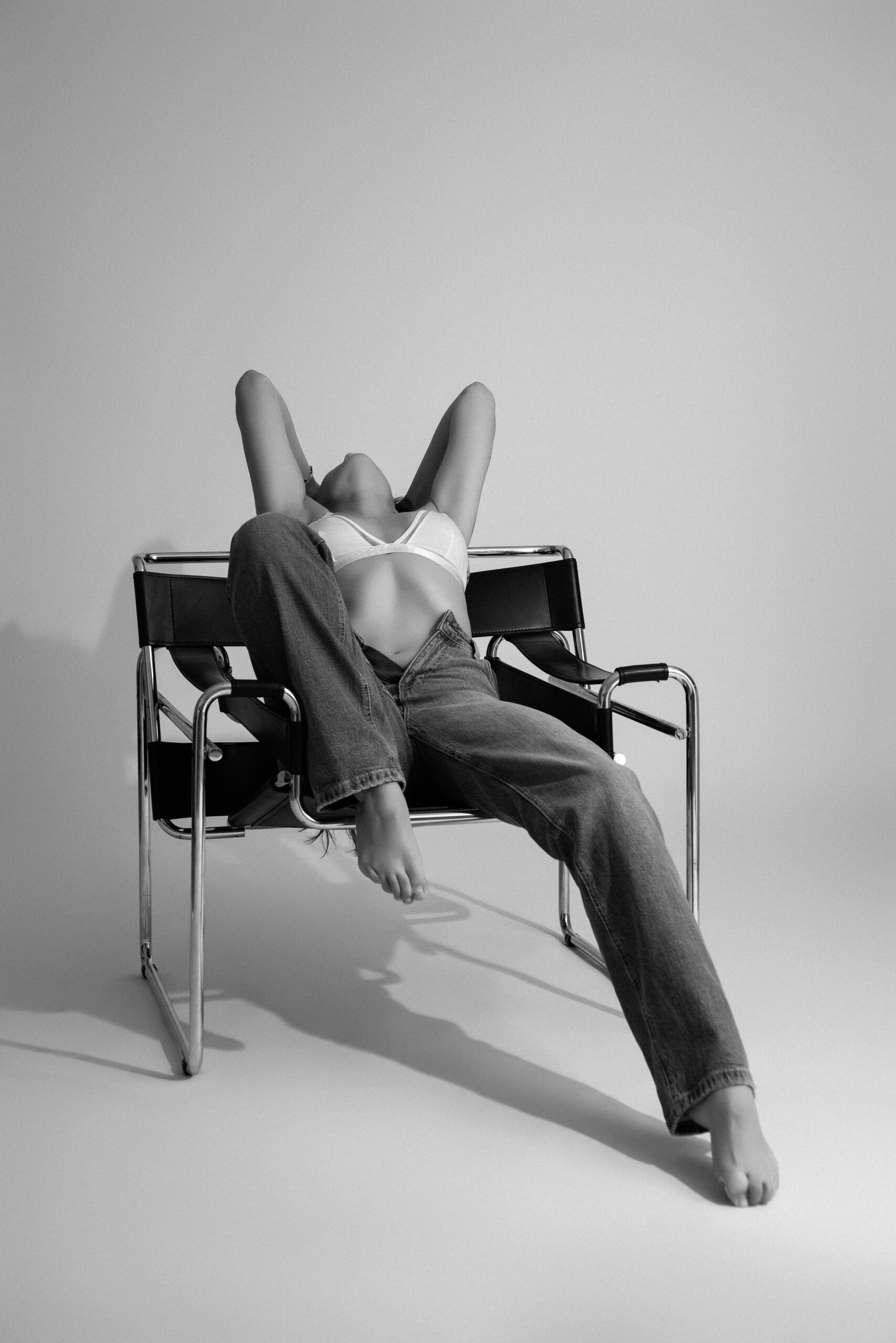 Kreatives Boudoir Shooting einer Frau in Jeans und BH auf Designstuhl im Fotostudio