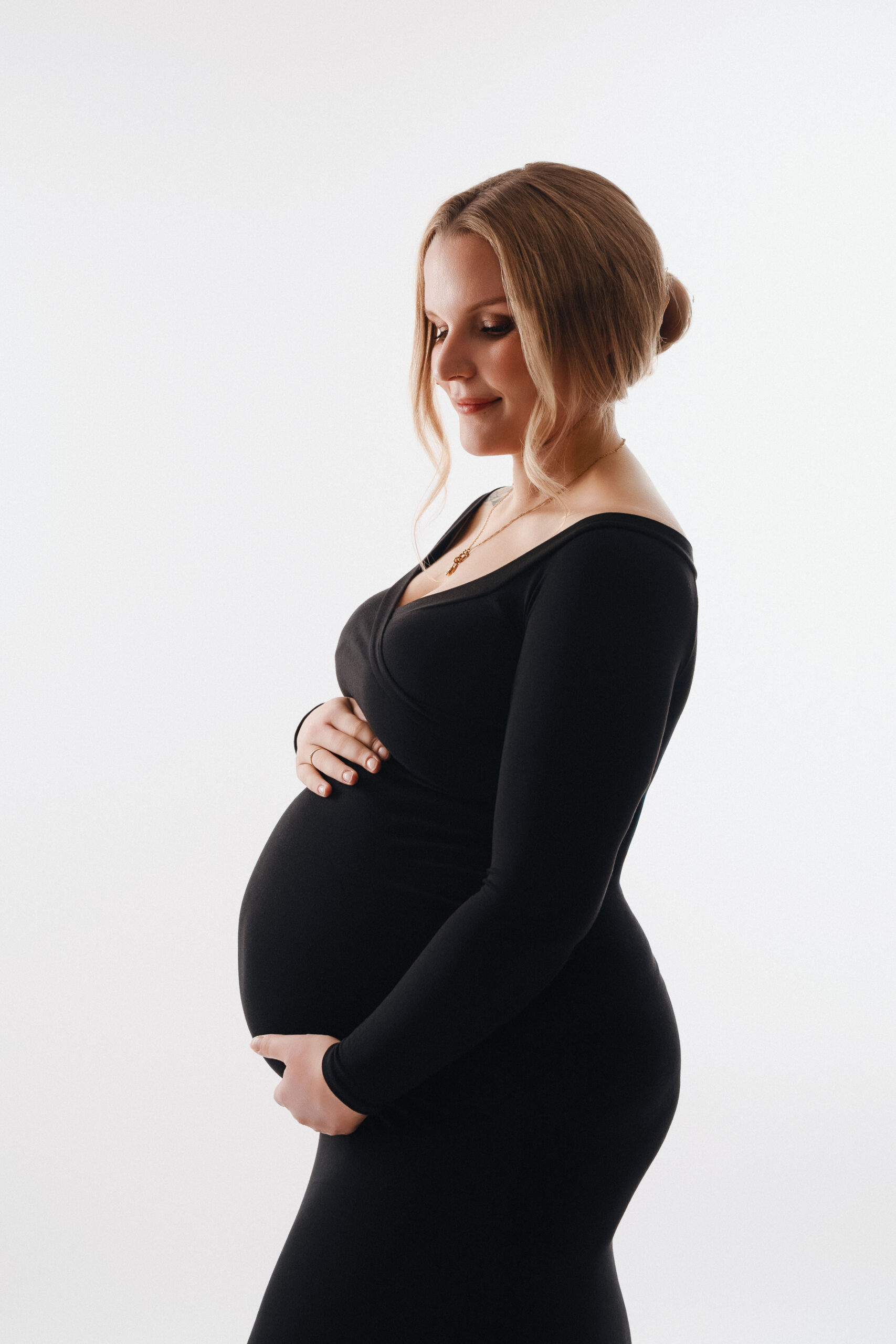 Schwangerschaft Fotoshooting in Ulm – elegante Babybauchaufnahme im schwarzen Kleid vor hellem Hintergrund
